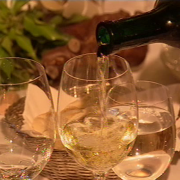 Nahaufnahme dreier Weingläser von denen eines gerade aus einer Flasche mit Weißwein gefüllt wird