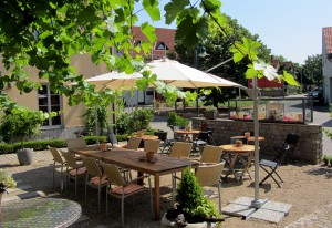 Blick in den sommerlichen Weinhof mit Holztischen, Stühlen und Sonnenschirmen auf Kiesgrund
